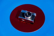 Зверху ретро фотокамера розміщена на металевому червоному колі на синьому фоні — стокове фото