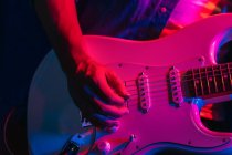 Crop guitariste masculin anonyme jouant de la guitare électrique en club avec néon violet et lumières bleues — Photo de stock