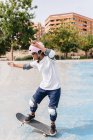 Full body of young ethnic person in casual outfit wearing protective helmet with knee pads and elbow pads riding skateboard in skate park — Stock Photo