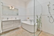 Interior moderno de baño minimalista con cabina de ducha y bañera de cerámica blanca cerca del lavabo y el espejo - foto de stock