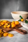 Pile of fresh orange cut kumquats on wooden chopping board placed on marble table with towel in kitchen — Stock Photo
