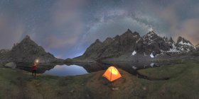 Picturesque scenery of unrecognizable traveler standing with bright light in hand near tent placed among rocky mountains under cloudless night sky milky way located in Circo de Gredos cirque in Spain — Stock Photo