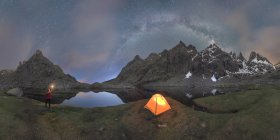 Cenário pitoresco de viajante irreconhecível de pé com luz brilhante na mão perto da barraca colocada entre montanhas rochosas sob céu noturno sem nuvens Via leitosa localizada no Circo de Gredos circo na Espanha — Fotografia de Stock