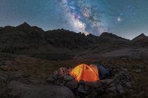 Scenic view of tent on lake shore against snowy mountain under cloudy milky way sky in evening located in Circo de Gredos cirque in Spain — Stock Photo