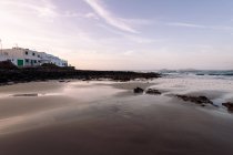 Famara Strand gegen Meer mit Bergen und Hausfassade unter bewölktem Himmel in Teguise Lanzarote Kanarische Inseln Spanien — Stockfoto