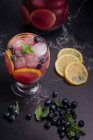 Alto ángulo de vidrio y jarra con refrescante limonada fría con arándanos frescos y rodajas de limón colocadas sobre una mesa oscura - foto de stock