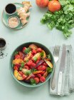 Vista superior de una ensalada de tomate crudo con fruta en una mesa con mantel verde rodeado de ingredientes saludables - foto de stock