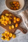 Top view pile of fresh orange cut kumquats on wooden chopping board placed on marble table with towel in kitchen — Stock Photo
