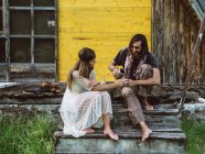 Hippie hombre vertiendo café o té de un termo a una taza sostenida por una hermosa mujer hippie en un porche de madera - foto de stock