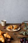 Leckere frisch gebackene Croissants serviert auf Teller mit Früchten in der Nähe Tasse Tee auf Holztisch in der Morgenzeit in hellen Raum platziert — Stockfoto