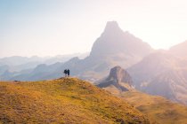 Entfernte anonyme Wanderer stehen auf grasbewachsenen Hügeln und bewundern raue Gebirgsketten vor wolkenlosem Himmel in der Natur Spaniens — Stockfoto