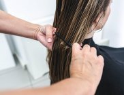 Vista lateral de anônimo jovem mulher penteando mestre com cabelos longos no salão de cabeleireiro — Fotografia de Stock