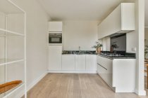Прості білі шафи з побутовою технікою, розташовані в світлій сучасній кухні нової квартири — стокове фото