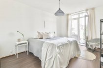 Interieur des zeitgenössischen Schlafzimmers mit weichem Bett und hölzernem Nachttisch in minimalistischem Stil in flacher — Stockfoto