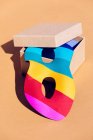 Maschera multicolore mascherata per evento festivo collocata in scatola di cartone aperta con coperchio su sfondo arancione in leggero studio moderno — Foto stock