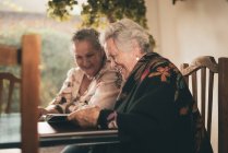 Irmãs idosas inspecionando fotos em álbum de fotos e discutindo memórias enquanto se sentam à mesa em casa juntas — Fotografia de Stock