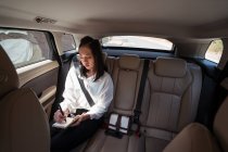 От серьезной женщины в формальной одежде в блокноте во время езды на пассажирском заднем сиденье в удобном такси — стоковое фото