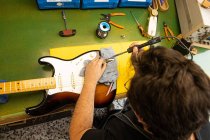 From above crop anonymous male luthier master using screwdriver while fixing electric guitar on table in light workshop — Stock Photo