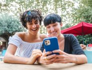 Дружелюбные к содержанию многорасовые женщины, просматривающие мобильный телефон, наслаждаясь вместе выходными в летнем парке — стоковое фото