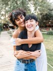 Pareja multiétnica amorosa positiva de mujeres homosexuales abrazándose con los ojos cerrados mientras están de pie en el camino en el parque de verano - foto de stock