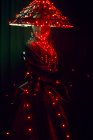 Неузнаваемая загадочная женщина в креативном традиционном наряде и вьетнамской головной убор с красной подсветкой, стоящая в темной студии на черном фоне во время выступления — стоковое фото
