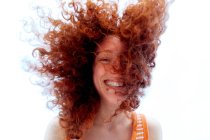 D'en bas jeune femme ravie couvrant le visage avec des cheveux roux bouclés tout en riant joyeusement en regardant la caméra — Photo de stock