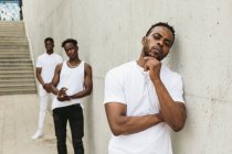Круті афроамериканські чоловіки чоловіки друзі одягнені в модний одяг з білою футболкою стоячи біля будівлі і дивлячись на камеру — стокове фото