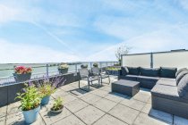 Veranda mit Sofa gegen Sessel und Topfpflanzen unter wolkenlosem blauen Himmel an sonnigen Tagen — Stockfoto