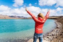 Back view of calm unrecognizable traveler standing on edge of cliff above blue ocean against mountains in Iceland in sunny day — Stock Photo