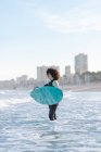 Vue latérale de la jeune surfeuse en combinaison sur l'eau de mer ondulante avec planche profitant de la journée d'été — Photo de stock