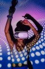 Mulher na moda no topo da colheita experimentando a realidade virtual no fone de ouvido enquanto dança em luzes do projetor — Fotografia de Stock