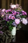 Buquê de peônias coloridas frescas e crisântemos em vaso branco colocado sobre mesa de madeira em quarto escuro — Fotografia de Stock