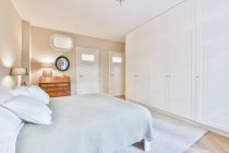 Cama com tampa e travesseiros contra portas e armário branco em casa com lâmpadas e espelho — Fotografia de Stock