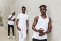Coole afroamerikanische Freunde in trendiger Kleidung mit weißem T-Shirt stehen in der Nähe des Gebäudes und schauen in die Kamera — Stockfoto