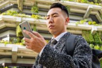 From below young ethnic male entrepreneur with tie looking at screen while speaking on cellphone in town — Stock Photo