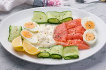 Dall'alto di salmone affumicato e formaggio fresco servito su piatto con uova sode e fette di cetriolo per pranzo saporito — Foto stock