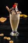 Склянка солодкого бананового молочного коктейлю, прикрашена збитими вершками і вишнею з шоколадом зверху — стокове фото