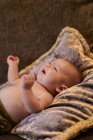 Alto ângulo de adorável chateado bebê sem camisa chorando enquanto deitado em almofada macia no sofá confortável em casa — Fotografia de Stock