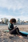 Positive Frau mit lockigem Haar trägt Neoprenanzug und surft mit Surfbrett am Sandstrand — Stockfoto
