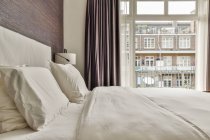 Komfortables Bett und minimalistischer Kleiderschrank in der Nähe des Fensters mit Vorhängen im modernen Schlafzimmer — Stockfoto