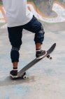 Анонімна молода етнічна особа в повсякденному вбранні в захисних колінних прокладках, що їздять в скейтборді в скейтборді парку — стокове фото