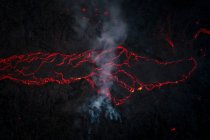 Вид сверху на горячую красную магму, текущую по темной горной поверхности ночью в высокогорье Исландии в темноте — стоковое фото