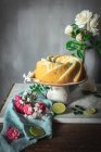 Bolo de esponja de limão saboroso servido em prato branco perto de flores e fatias de limão — Fotografia de Stock