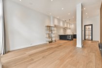 Interno della spaziosa cucina con mobili minimalisti neri in appartamento moderno con pareti bianche, pavimento in parquet e colonne in legno — Foto stock