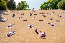 Instrutor de ioga em activewear sentado na posição de lótus, enquanto as pessoas deitadas em tapetes no chão durante Shavasana no parque em dia ensolarado — Fotografia de Stock