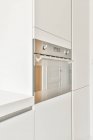 Вбудована хромова піч, встановлена в білі шафи на сучасній кухні з мінімалістичним інтер'єром — стокове фото