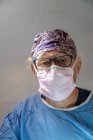 Anciano cirujano en máscara protectora y uniforme con sombrero trabajando en quirófano durante la cirugía - foto de stock