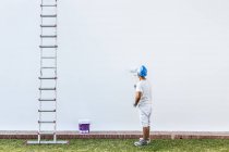 Невпізнаваний молодий живописець малює фасад квартири з валиком зі сходами збоку — стокове фото