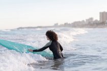 Vue latérale de la jeune surfeuse en combinaison sur l'eau de mer ondulante avec planche profitant de la journée d'été — Photo de stock