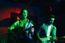 Man playing guitar while woman singing and performing song in club with neon lights — Stock Photo
